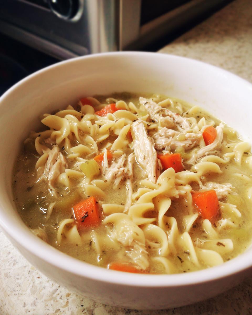 Close-up of a white bowl filled with Quick Creamy Chicken Noodle Soup, featuring egg noodles, shredded chicken, and carrots.