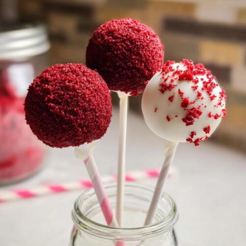 Three Red Velvet Cake Pops, two fully coated in red crumbs and one dipped in white chocolate with red sprinkles.