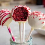 Three Red Velvet Cake Pops dipped in white chocolate, one showing the rich red interior texture.