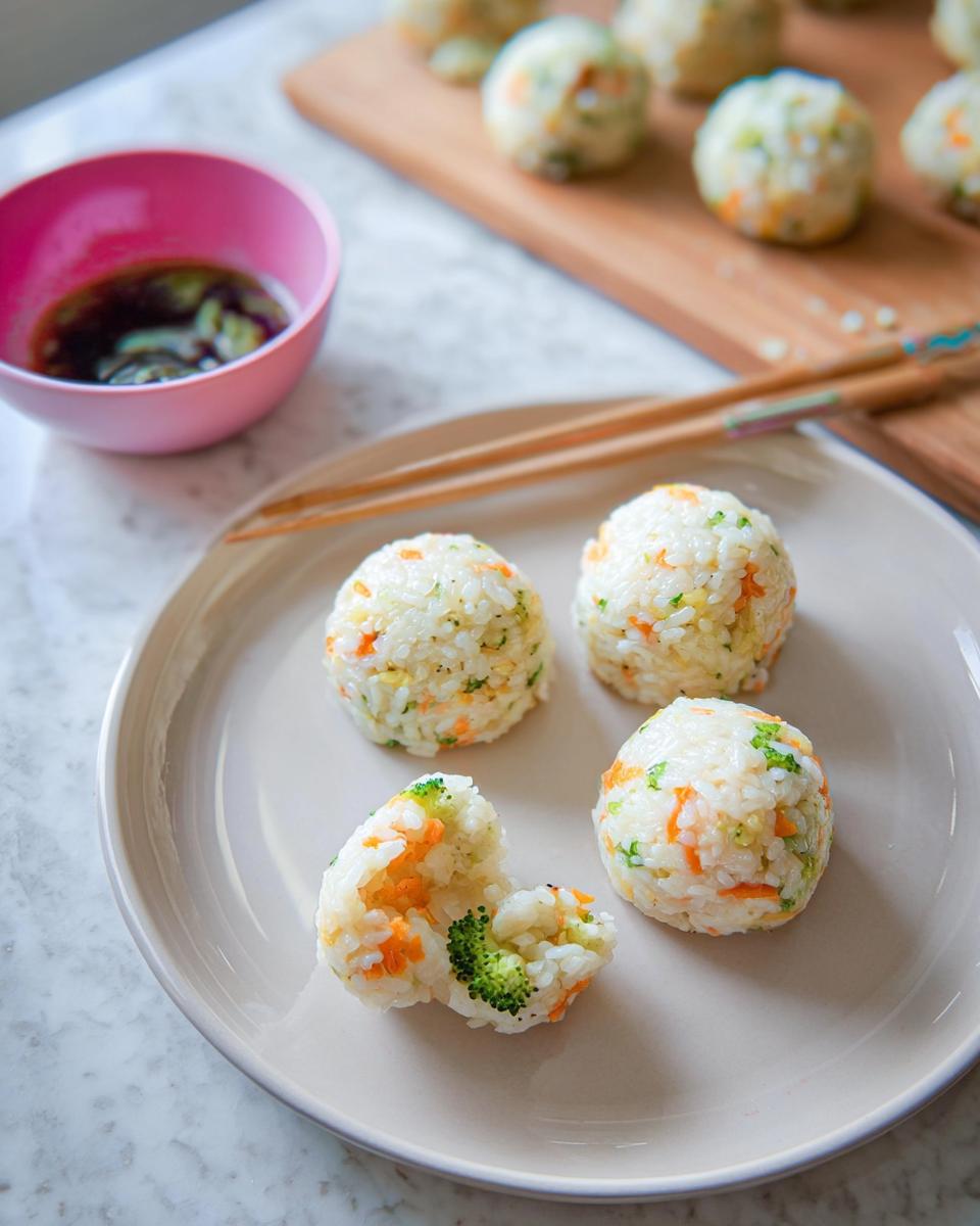 Four homemade Rice Ball Sushi Lunch portions on a plate, one broken open showing broccoli and carrots inside.