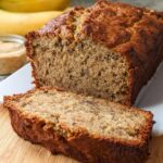 A close-up of a Rich Banana Sour Cream Loaf, sliced open to show the moist crumb, resting on a white platter.