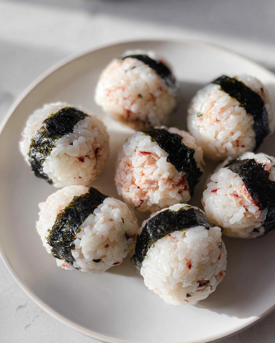 Seven perfectly formed Tuna Sushi Ball Recipe portions arranged on a white plate, each wrapped with a strip of dark nori seaweed.