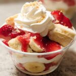 Close-up of a single serving Party Strawberry Banana Dessert in a clear cup, topped with whipped cream.