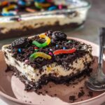 A square slice of creamy Birthday Dirt Cake topped with crushed cookies, sprinkles, and gummy worms on a pink plate.