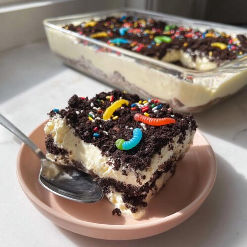 A square slice of creamy Birthday Dirt Cake topped with chocolate crumbs and colorful gummy worms.