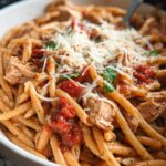 A close-up shot of a hearty Slow Cooker Chicken Pasta Dinner topped with shredded Parmesan cheese and fresh herbs.