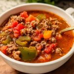 Close-up of a white bowl filled with rich Slow Cooker Pepper Soup featuring ground meat, diced tomatoes, and green peppers.