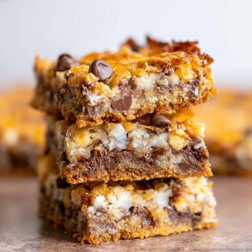 Close-up of three stacked, gooey 7-Layer Bars showing chocolate chips and coconut layers.
