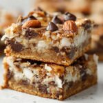 Two stacked squares of Classic Magic Cookie Bars showing layers of chocolate chips, coconut, and pecans on a graham cracker crust.