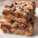 Two stacked Coconut Chocolate Chip Bars showing a thick base, melted chocolate, and toasted coconut topping.