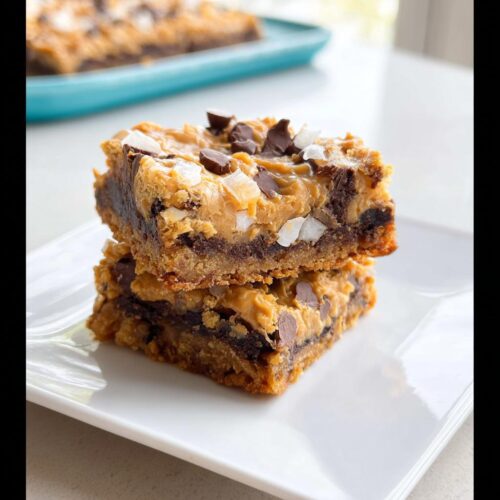 Two stacked Peanut Butter Magic Bars showing layers of crust, chocolate, peanut butter, coconut, and chocolate chips.