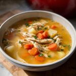 Close-up of a steaming bowl of Chicken Soup for Fall Dinners with shredded chicken, carrots, and potatoes.