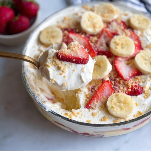 A spoonful of creamy Strawberry Banana Cream Dessert topped with crushed cookies and fruit.
