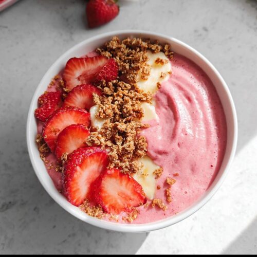 A vibrant Strawberry Banana Protein Smoothie Bowl topped with fresh strawberry slices, banana chunks, and granola.