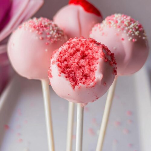 Close-up of four pink coated Strawberry Cake Pops, one showing the bright red cake interior after a bite was taken.