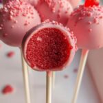 Close-up of Strawberry Cake Pops, showing the vibrant red cake interior of one cut pop.