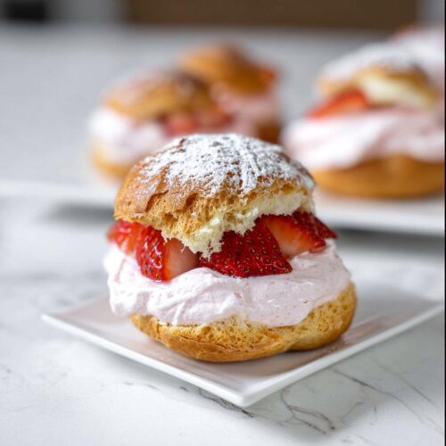 A single, delicious Strawberry Cream Puff filled with pink cream and fresh sliced strawberries, dusted with powdered sugar.