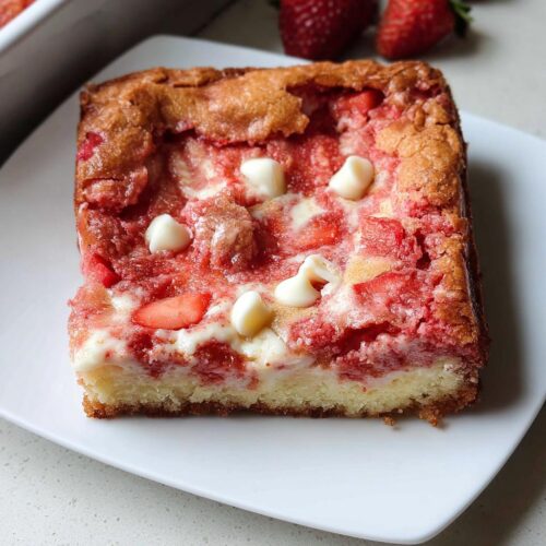 A square slice of Strawberry Earthquake Cake featuring a moist cake base, swirled strawberry filling, and white chocolate chips.