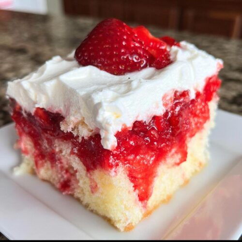 A square slice of Strawberry Poke Cake showing moist yellow cake soaked in strawberry filling, topped with whipped cream and a fresh strawberry.