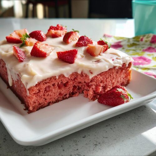 A moist slice of pink Strawberry Sheet Cake topped with white frosting and fresh strawberry pieces.
