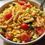 Close-up of a bowl filled with Summer Corn Pasta Meal Prep featuring penne, sweet corn, cherry tomatoes, and cucumber.