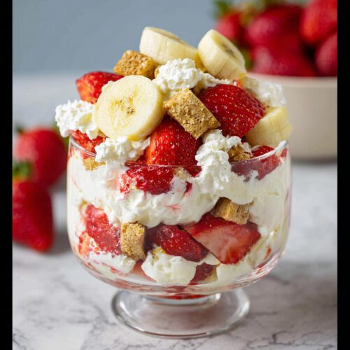 A layered Summer Strawberry Banana Dessert featuring fresh strawberries, banana slices, whipped cream, and graham cracker pieces.