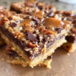 A close-up, stacked view of rich Toffee Magic Cookie Bars featuring a shortbread crust, chocolate, nuts, and gooey caramel topping.