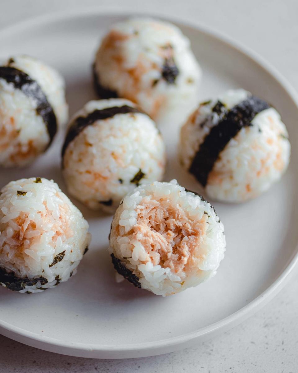 Close-up of several Tuna Sushi Ball Recipe portions on a white plate, one cut open showing the flaky tuna filling.