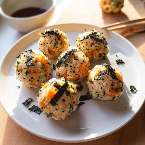 Six perfectly formed Vegetarian Sushi Balls mixed with carrots and cucumber, topped with nori and sesame seeds.