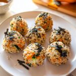 A plate holding seven perfectly formed Vegetarian Sushi Balls mixed with carrots, cucumber, sesame seeds, and topped with shredded nori.