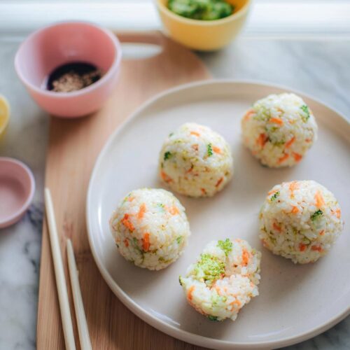 Five homemade Rice Ball Sushi Lunch portions mixed with visible carrots and broccoli on a light plate.