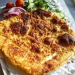 A golden-brown, slightly charred Viral Cottage Cheese Flatbread served with fresh cucumber, tomatoes, and red onion slices.