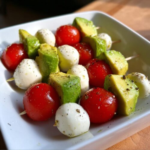 Close-up of Avocado Caprese Bites skewers featuring cherry tomatoes, mozzarella balls, and avocado chunks seasoned with pepper.