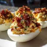 Four halves of Bacon Cheddar Deviled Eggs piled high with filling, topped generously with crispy bacon bits and chives.