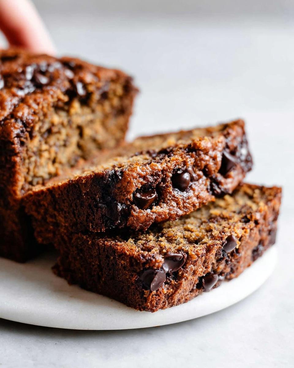 Two thick slices of moist Bakery-Style Chocolate Chip Banana Bread stacked on a white plate.