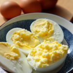 Four halves of Boiled Eggs with Butter and Salt served in a blue and white patterned bowl, with whole eggs in the background.