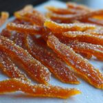 Close-up of glistening, sugary strips of Candied Orange Peel with Brown Sugar resting on a light surface.