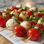 Close-up of Caprese Bites with Marinated Mozzarella, cherry tomatoes, and basil on skewers drizzled with balsamic glaze.