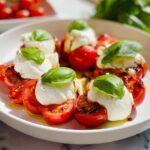 Close-up of several Caprese Bites with Burrata, featuring sliced tomatoes, creamy white burrata, and fresh basil leaves drizzled with balsamic.