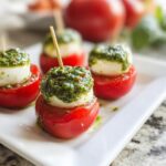 Four Caprese Bites with Pesto, featuring cherry tomatoes, mozzarella balls, and green pesto, skewered on toothpicks.