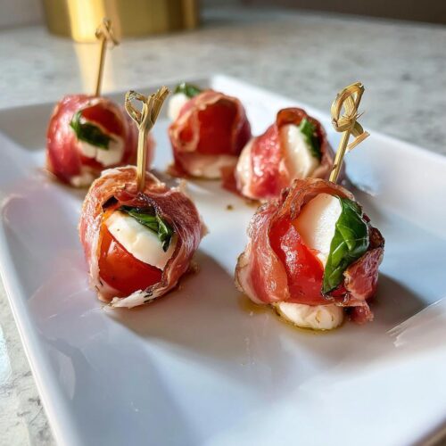 Close-up of Caprese Bites with Prosciutto wrapped around mozzarella, tomato, and basil, held with toothpicks.