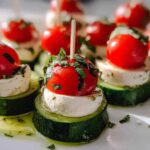 Close-up of stacked Caprese Cucumber Bites featuring cucumber, mozzarella, cherry tomato, and basil, drizzled with oil.