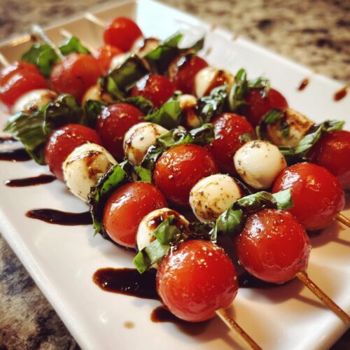 Close-up of several Caprese Skewers with Balsamic drizzled over cherry tomatoes, mozzarella balls, and basil leaves.