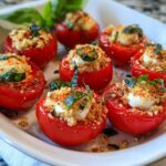 A white platter holding several bright red Caprese Stuffed Cherry Tomatoes topped with mozzarella and breadcrumbs.