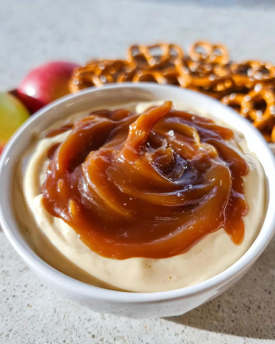 Close-up of a white bowl filled with Caramel Pretzel Dip topped with rich, swirled caramel sauce.