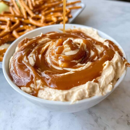 Close-up of Caramel Pretzel Dip in a white bowl, with caramel sauce being drizzled on top in a swirl pattern.