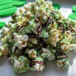 A festive pile of Chocolate Drizzle Leprechaun Popcorn covered in green and yellow sprinkles and drizzled with chocolate.