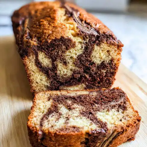 Close-up of a freshly baked Chocolate Swirl Banana Loaf, showing a slice cut away revealing the marbled chocolate and banana batter.