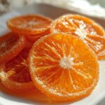 Close-up of several glistening Classic Candied Orange Slices coated in granulated sugar on a white plate.
