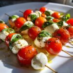 Close-up of several Classic Caprese Bites skewers featuring cherry tomatoes, mozzarella balls, and basil leaves drizzled with pesto.